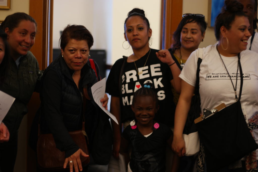 group of people, including a young child, gather inside City Hall as they visit politicians offices to demand housing and services for homeless families.