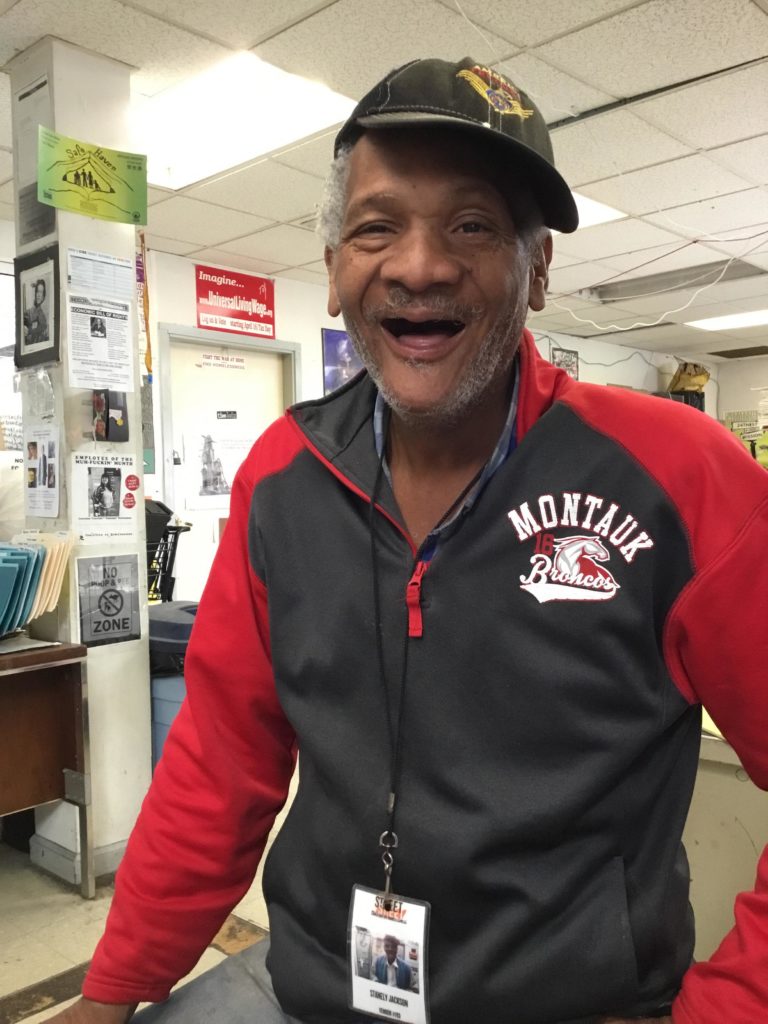 A smiling Street Sheet vendor sits on a desk wearing his vendor badge