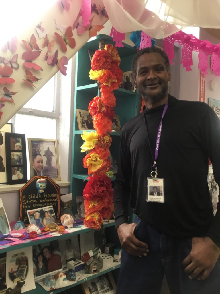 Street Sheet vendor Tariq Johnson stands in the Coalition on Homelessness office wearing his vendor badge on a landyard and grinning.