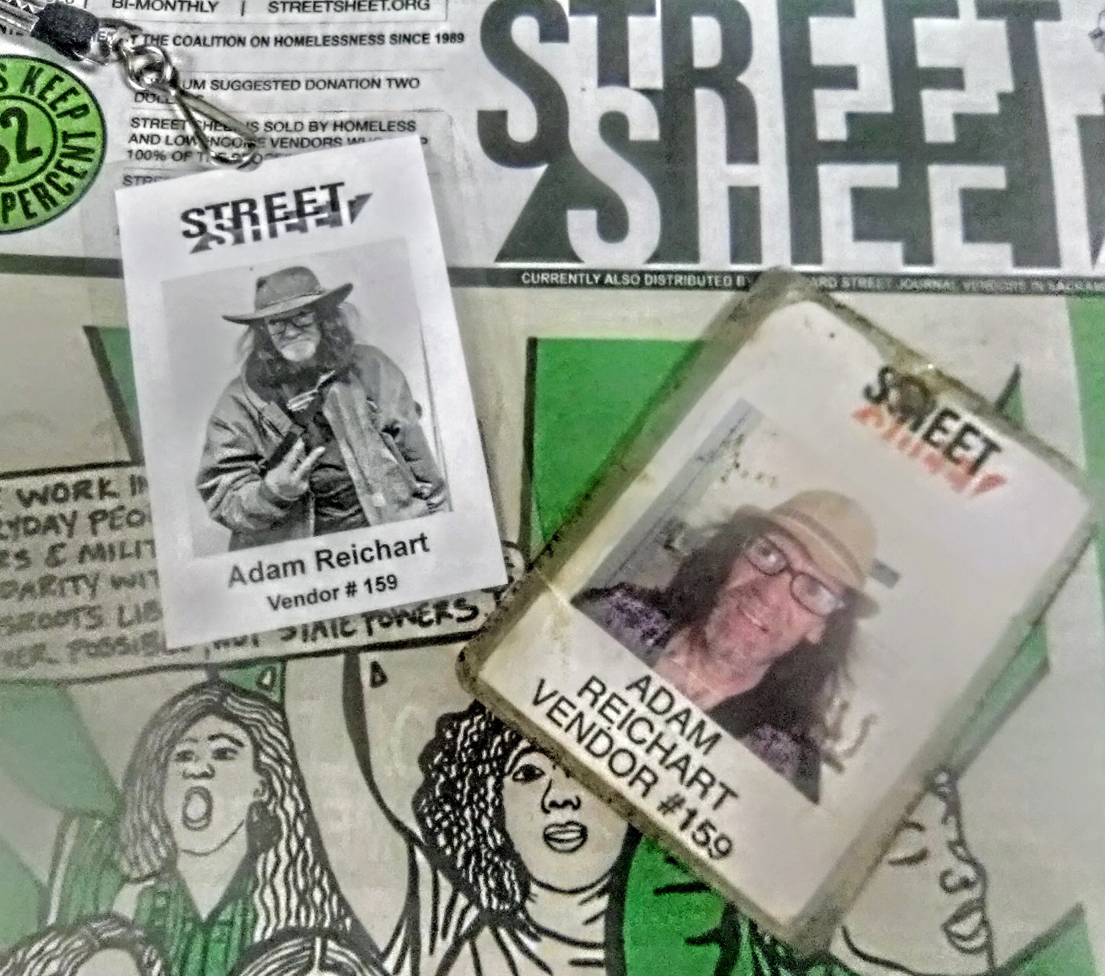Vendor badges of Adam Reichart with his photo and buade number 159 lying on top of a copy of the Street Sheet newspaper